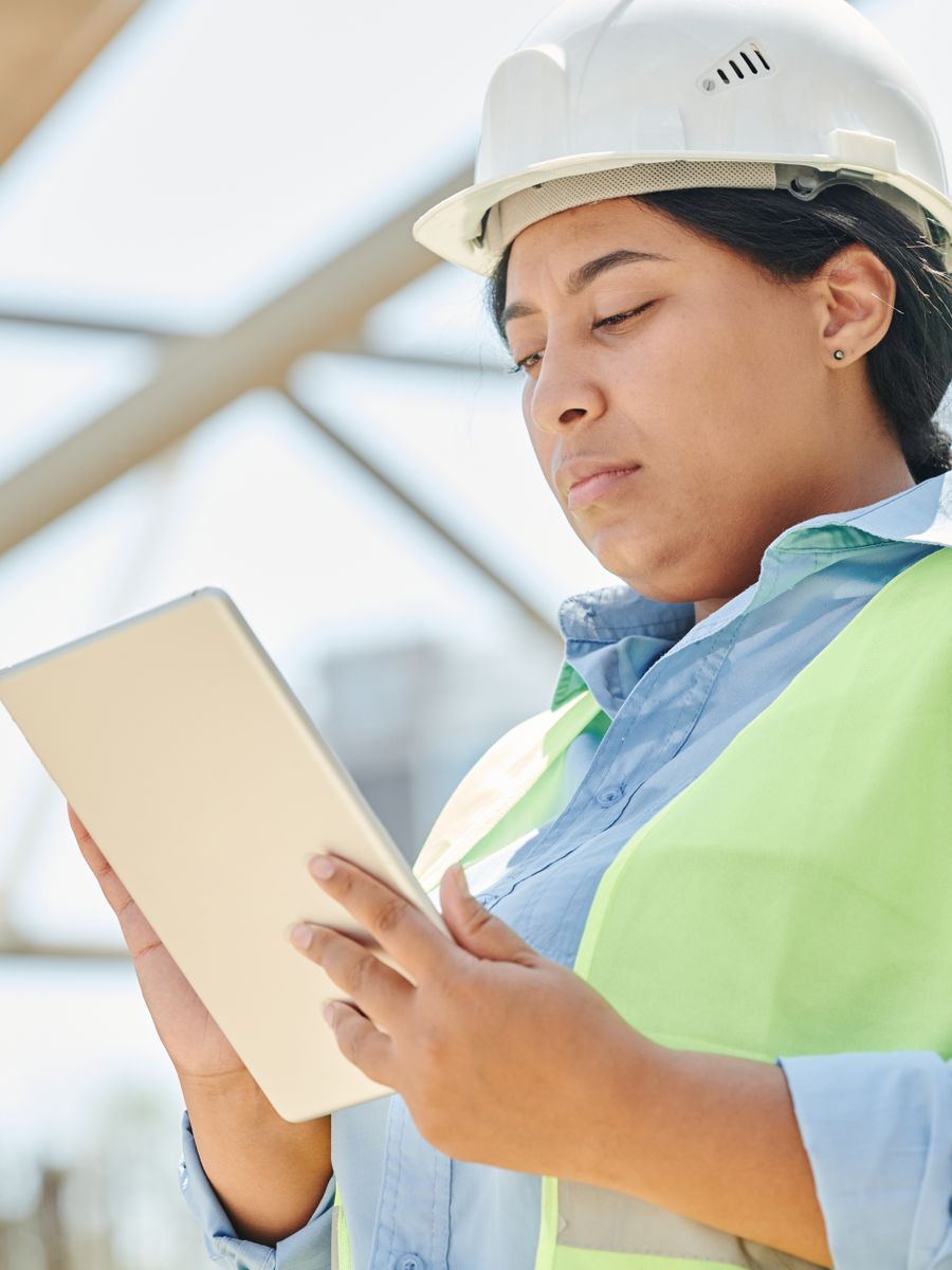 Site engineer in a hard hat and hi-vis vest working from a tablet on site
